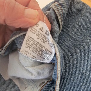 Puede incluir: Primer plano de unos vaqueros azules. Una etiqueta blanca muestra las instrucciones de lavado y los detalles de la talla. La etiqueta muestra las tallas 44 1/4 y 32 1/2. Los vaqueros est&aacute;n doblados, mostrando el bolsillo interior y las costuras.