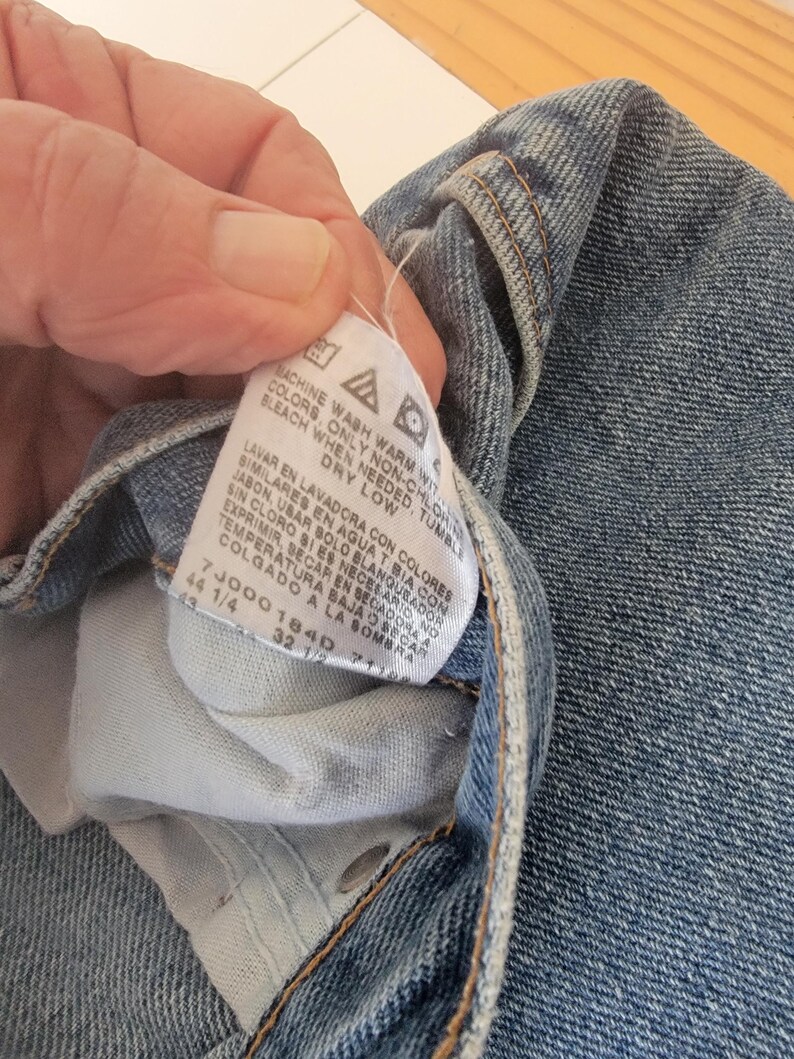 Puede incluir: Primer plano de unos vaqueros azules. Una etiqueta blanca muestra las instrucciones de lavado y los detalles de la talla. La etiqueta muestra las tallas 44 1/4 y 32 1/2. Los vaqueros est&aacute;n doblados, mostrando el bolsillo interior y las costuras.