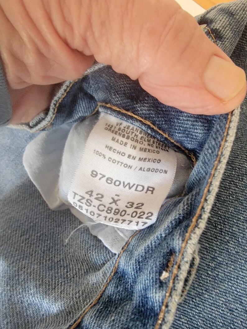 Puede incluir: Primer plano de una etiqueta de vaqueros de mezclilla azul claro. La etiqueta dice "VF Jeanswear, Greensboro, NC, Made in Mexico, 100% Cotton". Los vaqueros son de talla 42 x 32.