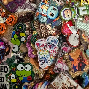 May include: A collection of assorted acrylic charms featuring various cartoon characters, animals, and group photographs. Each piece is finished with a glittery border, showcasing vibrant colors and detailed illustrations of figures like Winnie the Pooh, Buzz Lightyear, and dalmatian puppies.