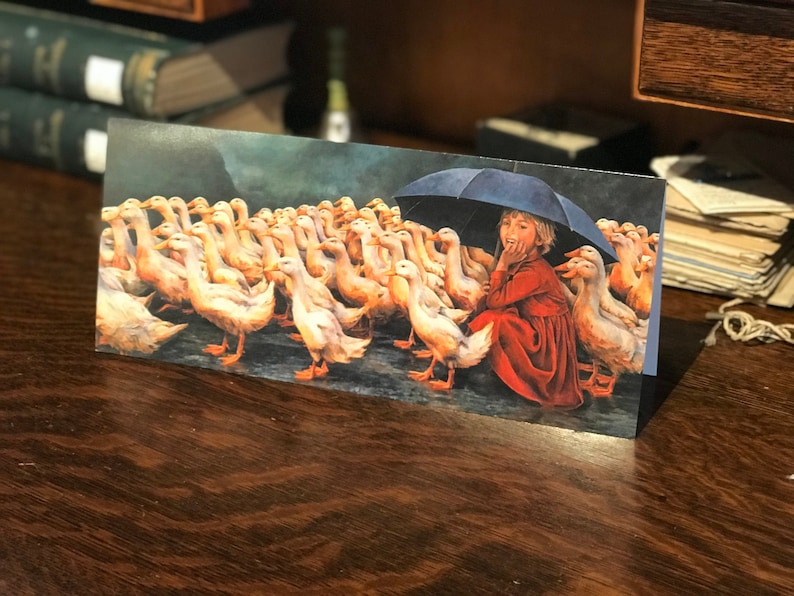 May include: A young girl in a red dress sits under a blue umbrella with a flock of white ducks surrounding her. The ducks are all facing the girl, and she is looking at them with a smile on her face.