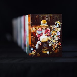 May include: A girl in a pink dress and a straw hat sits in a chair reading a book. She is surrounded by a variety of whimsical creatures, including a bird, a rabbit, and a squirrel. The scene is set in a library with bookshelves filled with books.