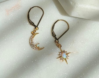 May include: A pair of gold earrings with a crescent moon and a star design. Each earring features a small opal gemstone and is adorned with sparkling cubic zirconia stones.