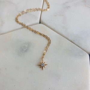 May include: A gold chain necklace with a small, star-shaped pendant featuring a clear crystal in the center.