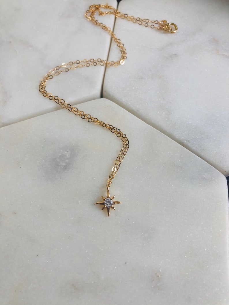 May include: A gold chain necklace with a small, star-shaped pendant featuring a clear crystal in the center.