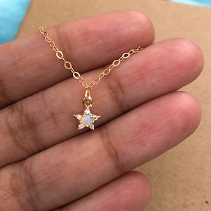 Op de afbeelding: Een gouden ketting met een klein stervormig hanger met een witte opaal steen omringd door heldere zirkonia stenen.