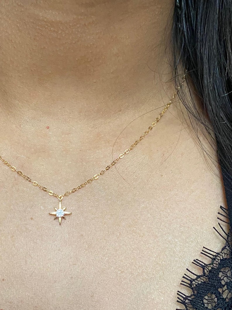 May include: A gold chain necklace with a small star pendant featuring a clear crystal in the center.