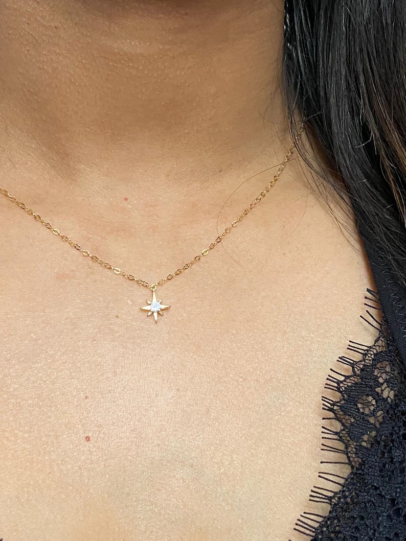 May include: A gold chain necklace with a small, star-shaped pendant featuring a clear stone in the center.
