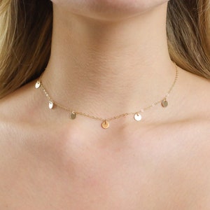 May include: A gold chain necklace with small, round, dangling charms. The necklace is worn by a person with long, blonde hair.