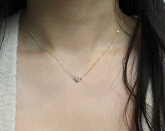 May include: A delicate gold chain necklace with a small, clear gemstone pendant.
