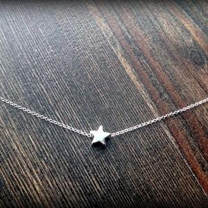 May include: A delicate silver chain necklace with a small, five-pointed star pendant.