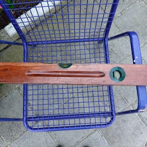 May include: A wooden spirit level with two green and yellow bubble vials. The level is resting on a blue metal chair.