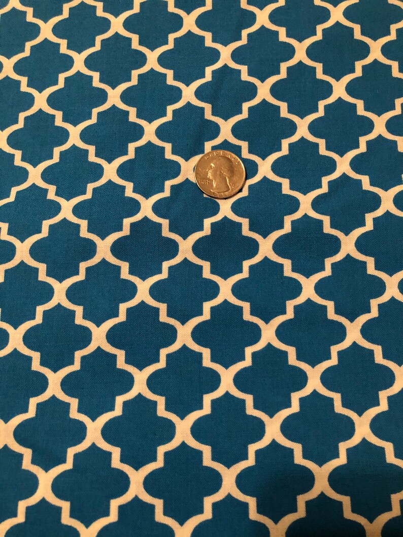 May include: Teal fabric with a repeating quatrefoil pattern in off-white. A U.S. quarter coin is placed on the fabric for scale. The fabric has a textured appearance and is likely cotton or a similar material.