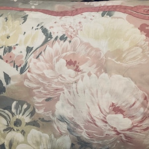 May include: A close-up of a fabric with a floral pattern. The fabric is a light pink color with white and gray flowers. The flowers are large and have a soft, watercolor-like appearance.