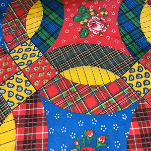 May include: Close-up of a colorful quilt with a patchwork design. The quilt features a variety of patterns, including plaid, paisley, and floral prints. The color palette includes red, yellow, blue, and green.