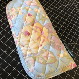 May include: A quilted blue eyeglass case with a floral pattern in shades of pink, yellow, and green. The case has a green label with the text "LAURA ASHLEY" on it.