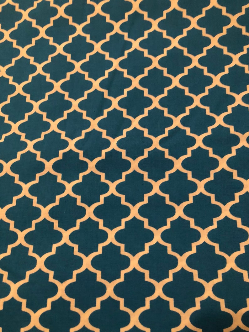 May include: A teal fabric with a repeating quatrefoil pattern in a cream color. The design is symmetrical and covers the entire surface, creating a visually appealing texture. This fabric is suitable for various craft projects.
