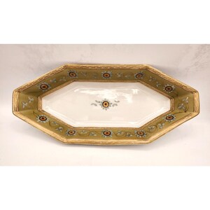 May include: A white octagonal serving dish with a gold rim and green floral design. The dish has a white center with a small floral design in the center.