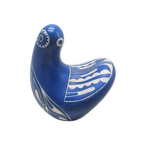 Może przedstawiać: Ceramiczna rzeźba stylizowanego ptaka w głębokim niebieskim kolorze. Ptak posiada białe wzory dekoracyjne na ciele i głowie, z okrągłym detalem oka. Rzeźba ma gładkie, błyszczące wykończenie i unikalny, zakrzywiony kształt.