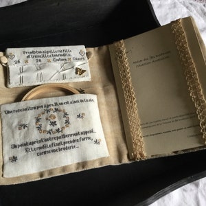 Peut inclure: Une pochette en tissu beige avec un cerceau à broder en bois, un étui à aiguilles et un petit livre intitulé "Atelier des Fees Brodeuses Collection Accessoires". La pochette contient une citation en français qui dit "Une rose naitra peu a peu. Il en est ainsi de la vie. Un point apres l'autre patiemment appose... Et le modele final prendra forme, comme une broderie..."
