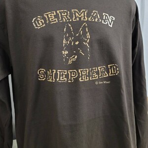 May include: A brown long-sleeve t-shirt with a tan graphic of a German Shepherd dog and the text "GERMAN SHEPHERD" in a distressed font. The text "&copy; Sew What!" is printed below the graphic.