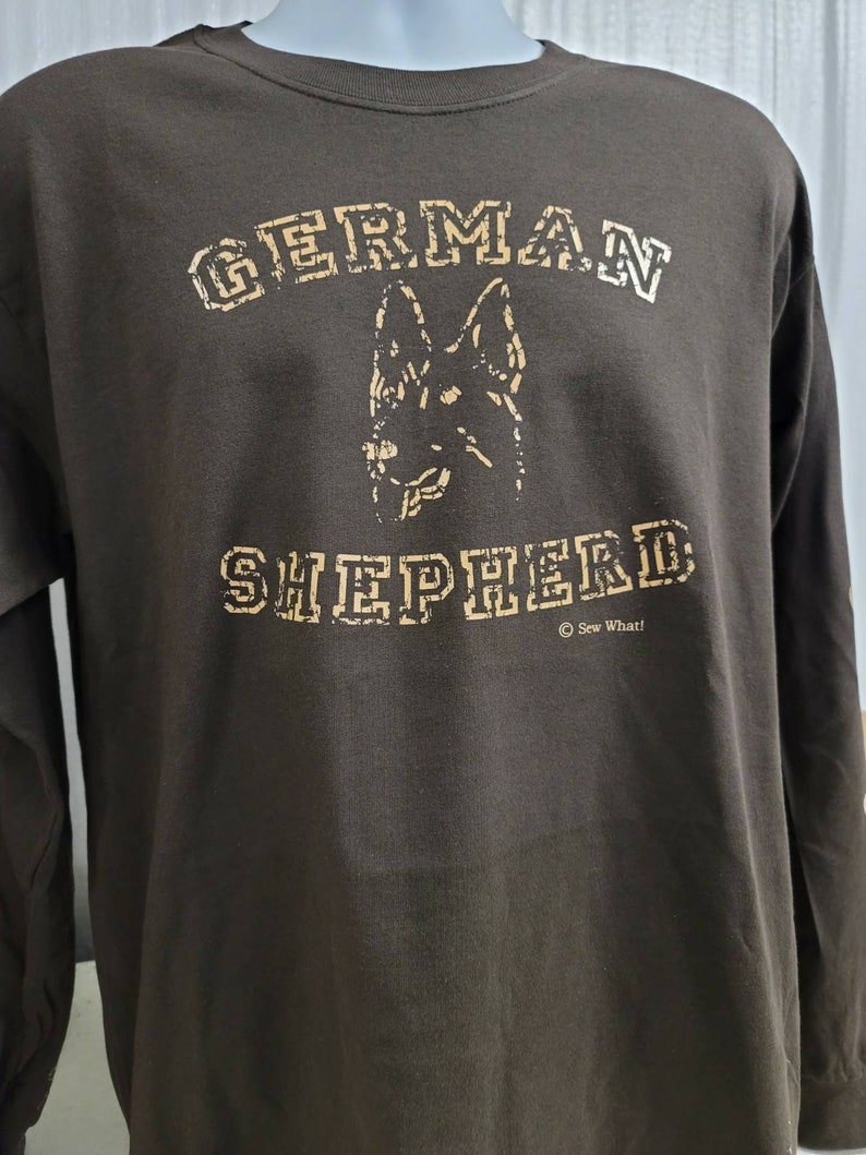 May include: A brown long-sleeve t-shirt with a tan graphic of a German Shepherd dog and the text "GERMAN SHEPHERD" in a distressed font. The text "&copy; Sew What!" is printed below the graphic.