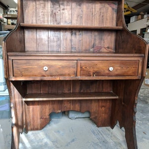 May include: A dark brown wooden hutch with two drawers and two shelves. The hutch has a curved top and bottom and is made of solid wood.