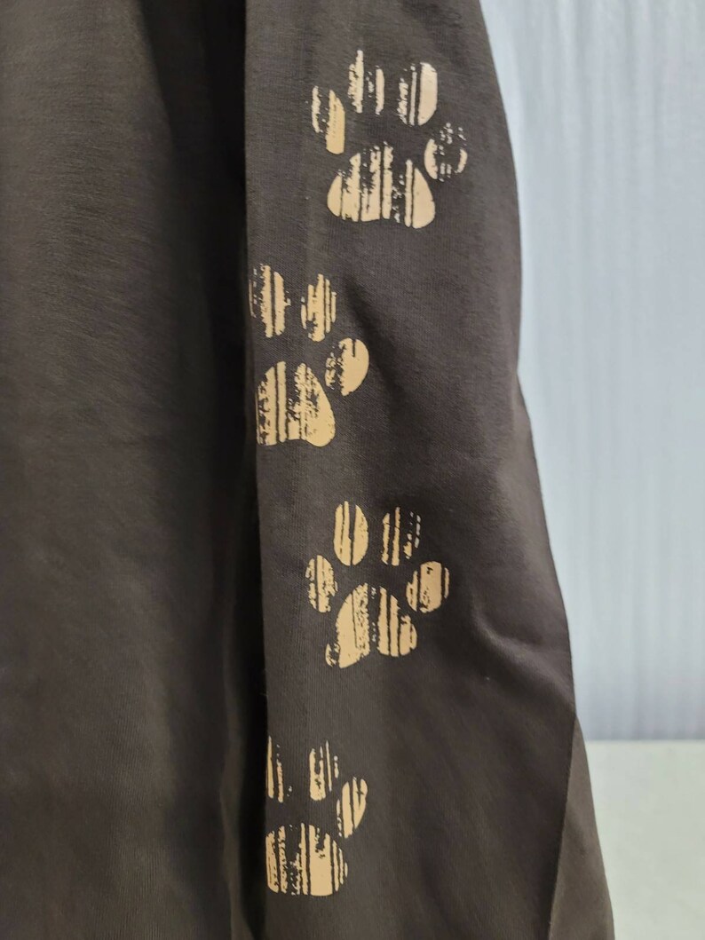 May include: A brown long-sleeved shirt with four paw prints on the sleeve. The paw prints are a light brown color and have a striped pattern.