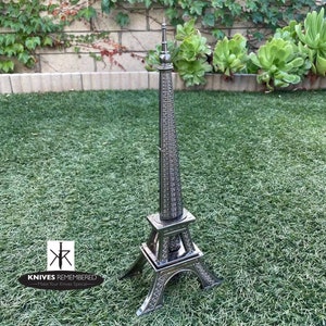 May include: A silver Eiffel Tower-shaped knife holder with the text "Knives Remembered - Make Your Knives Special" on the base.