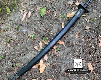 May include: A black leather-wrapped sword with a silver hilt and a skull and crossbones design on the pommel. The sword is lying on a bed of brown leaves and dirt. The text "Knives Remembered - Make Your Knives Special" is visible in the lower right corner of the image.