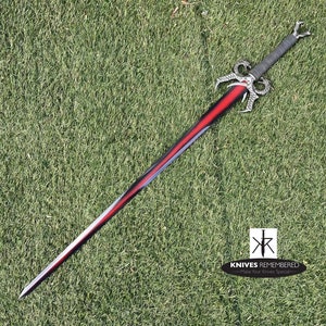 May include: A black and red sword with a silver handle and a dragon-like design. The sword is on a green grassy surface.