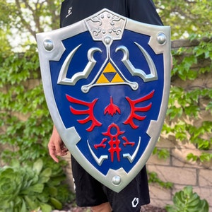 May include: A silver and blue shield with a red and yellow design. The shield has a triangular design with a winged symbol and a stylized figure.