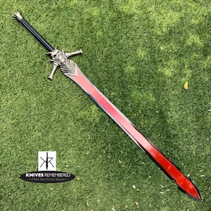 May include: A red and silver sword with a demon head design on the hilt. The sword is lying on a green grassy surface.