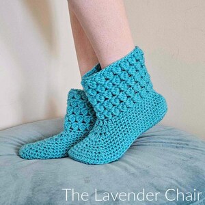 May include: A pair of teal blue crocheted slipper boots. The boots are made with a textured stitch and have a soft, cozy look.