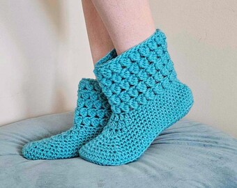 May include: A pair of teal blue crocheted slipper boots. The boots are made with a textured stitch and have a soft, cozy look.
