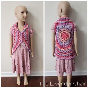 May include: A pink, purple and red crochet vest with a scalloped edge and a large crocheted flower on the back. The vest is being modelled by a child.