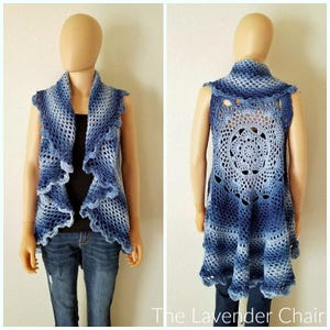Op de afbeelding: Een gebreid vest met een blauw en wit ombre patroon. Het vest heeft een gegolfde zoom en een grote gehaakte cirkel op de rug. Het vest is mouwloos en heeft een brede, open halslijn.