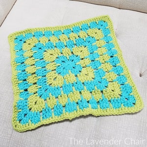 Puede incluir: Un cojín cuadrado de crochet con un patrón geométrico verde y azul. El cojín está hecho con un punto de granny square y tiene un borde simple.