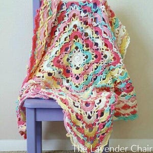 May include: A crocheted baby blanket in shades of pink, yellow, and blue with a white center. The blanket is draped over a purple chair.