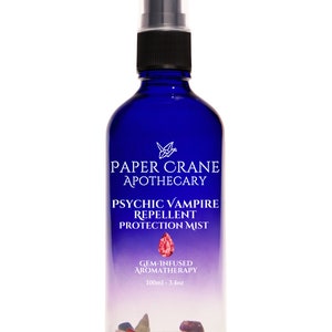 May include: A dark blue glass bottle with a black cap and spray nozzle. The bottle contains a purple liquid and has the text "PAPER CRANE APOTHECARY PSYCHIC VAMPIRE REPELLENT PROTECTION MIST". The bottle contains 3.4 oz of liquid.