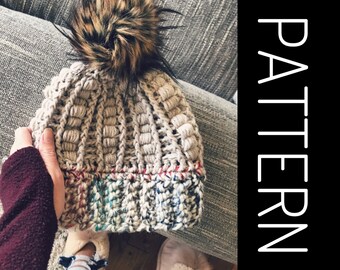 May include: A beige crochet beanie with a brown and black faux fur pom pom. The beanie has a colorful stripe at the bottom.