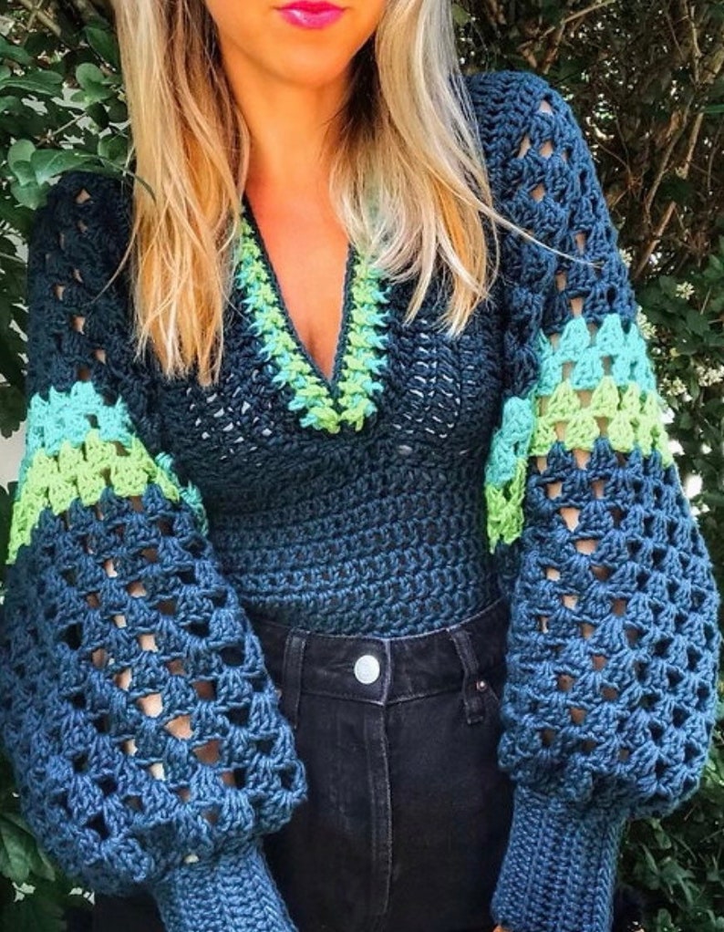 May include: A blue crochet sweater with green and blue stripes on the sleeves and a green and blue trim around the neckline.