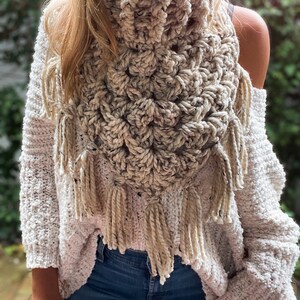 May include: A crocheted cream-coloured scarf with fringe. The scarf is made with a textured stitch and has a triangular shape.