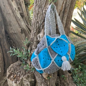 May include: A crocheted tote bag in grey and turquoise. The bag has a long grey handle and a small grey tassel.