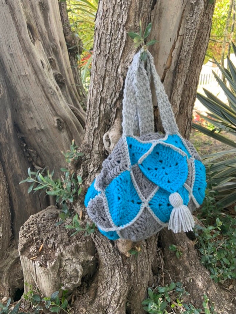 May include: A crocheted tote bag in grey and turquoise. The bag has a long grey handle and a small grey tassel.