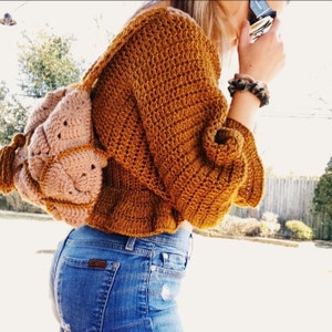 May include: A brown crocheted sweater with a loose fit and long sleeves. The sweater is worn over a pair of blue jeans.