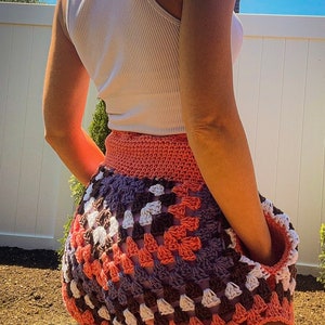 Puede incluir: Una falda de ganchillo con un patr&oacute;n de granny squares en tonos de rosa, blanco, marr&oacute;n y morado. La falda es corta y tiene un corte holgado.