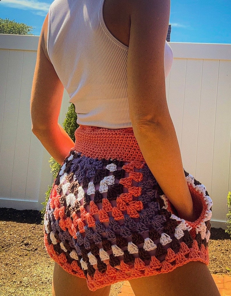 Puede incluir: Una falda de ganchillo con un patr&oacute;n de granny squares en tonos de rosa, blanco, marr&oacute;n y morado. La falda es corta y tiene un corte holgado.
