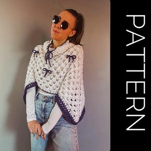 Puede incluir: Un poncho de crochet blanco con cuello alto y ribete morado oscuro. El poncho presenta lazos morados oscuros y un cordón. La palabra "PATTERN" está escrita verticalmente en blanco sobre un fondo negro.