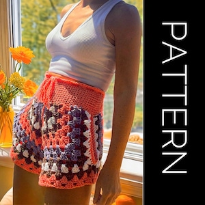 Puede incluir: Una falda de crochet con un patrón de cuadrados de la abuela en tonos de rosa, morado, blanco y marrón. La falda tiene una cintura con cordón y se muestra puesta con un top blanco sin mangas.